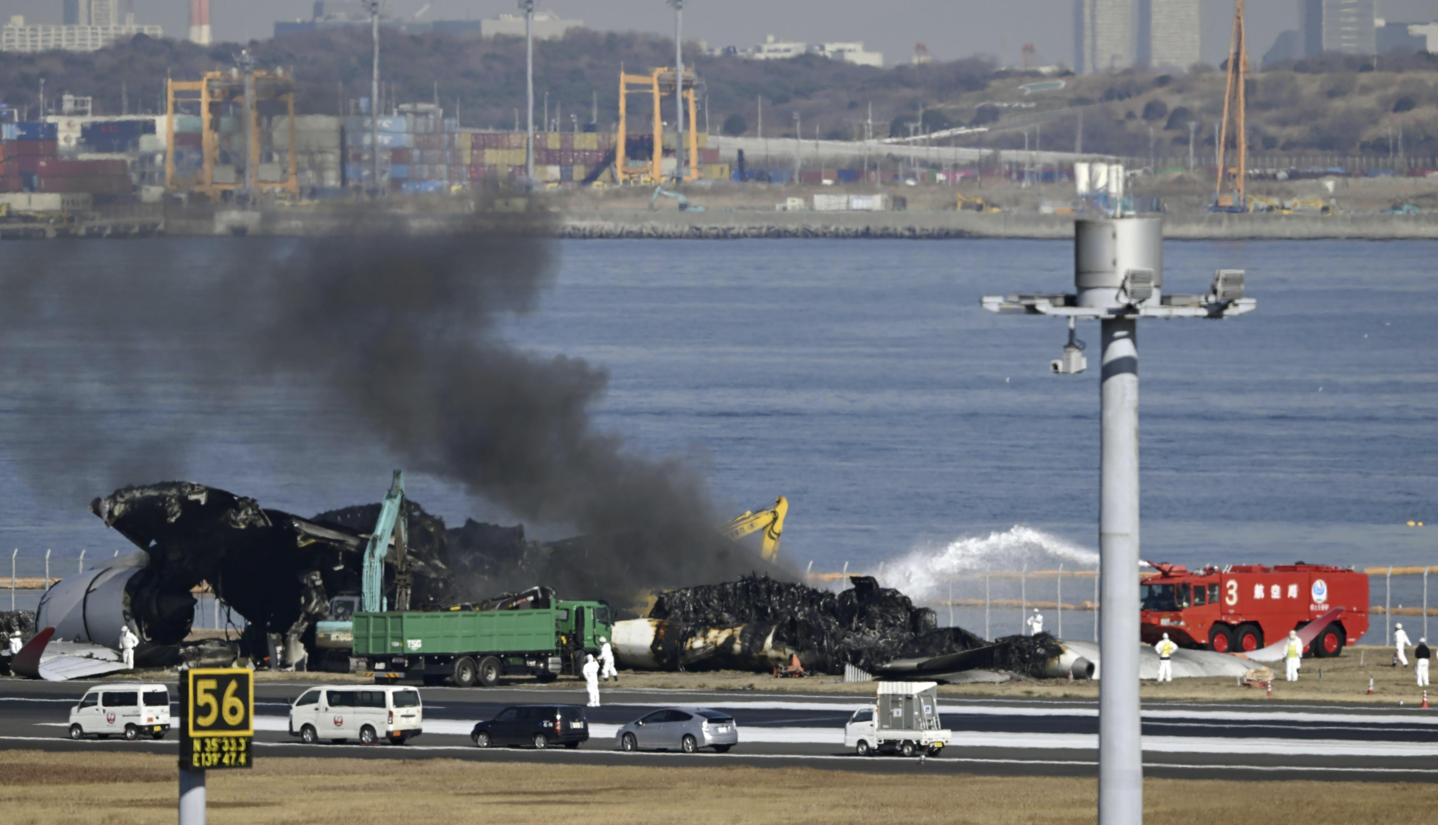 Black smoke rises while a removal work is underway at the site of a planes collision at Haneda airport in Tokyo Friday, Jan. 5, 2024. Cranes were dismantling the Japan Airlines Flight 516 Airbus A350 that caught fire after hitting a Coast Guard aircraft while it was landing Tuesday at the airport. (Kyodo News via AP)